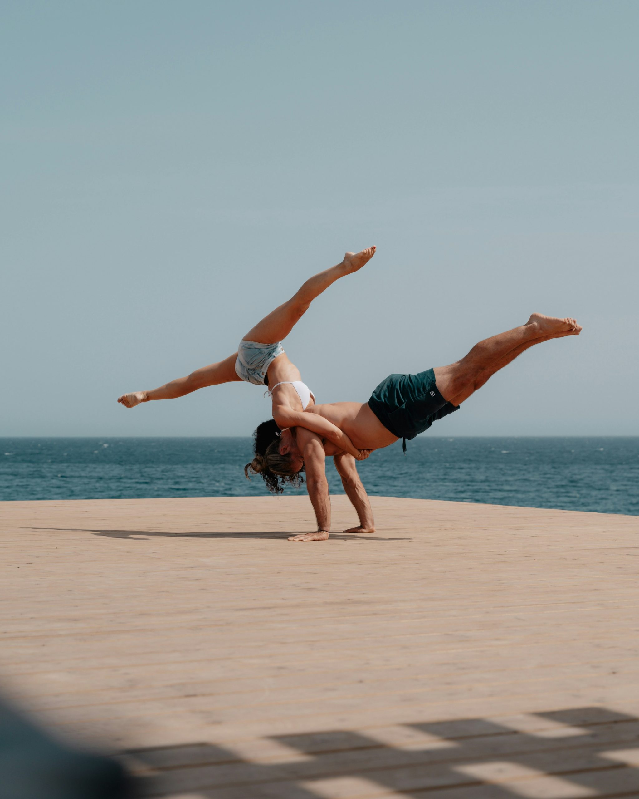 Zwei Leute am Strand kombinierte Yogaübung einer auf dem andern balance