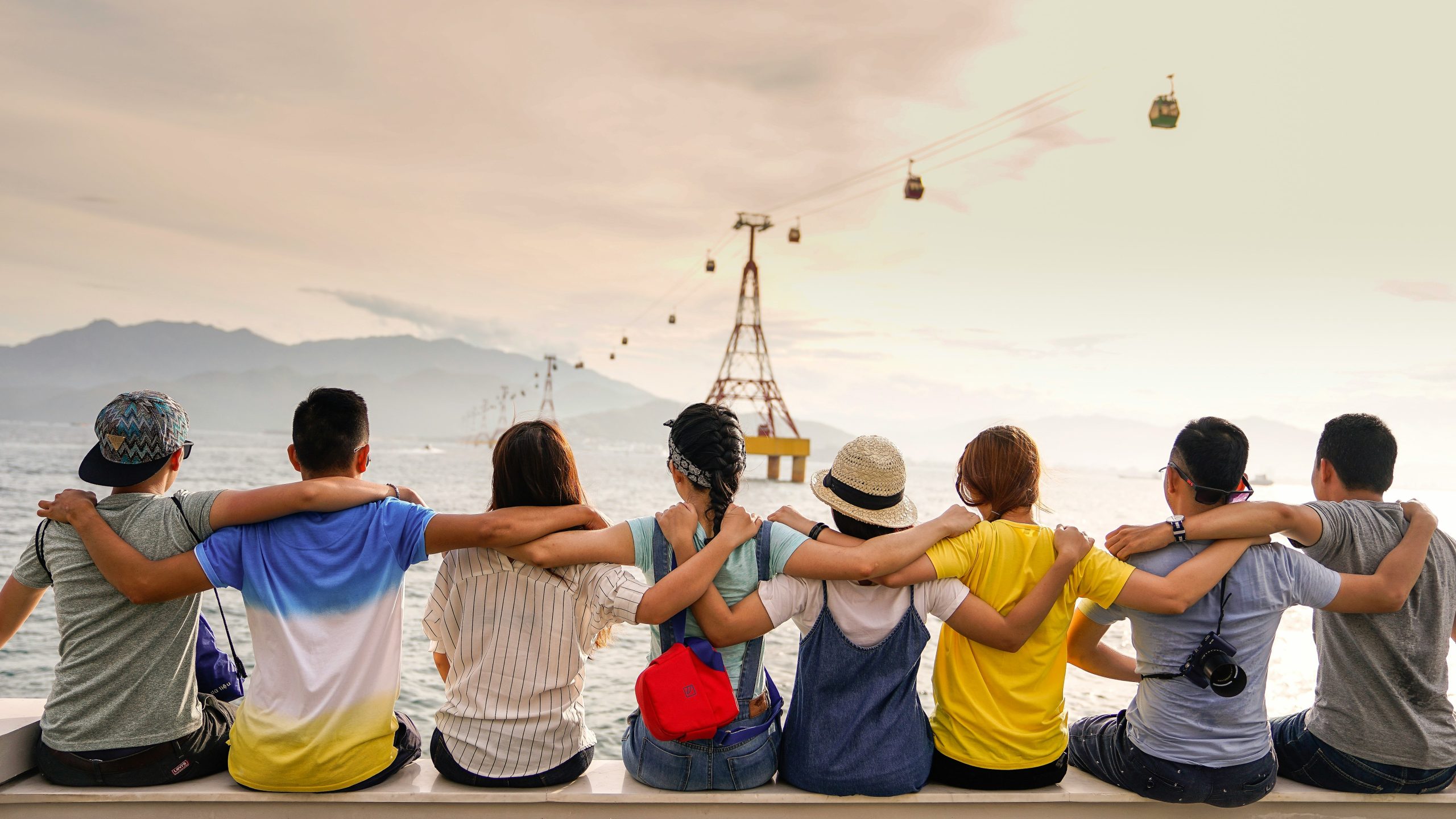 8 Leute die nebeneinander auf einer Kante sitzen udn aufs Meer schauen